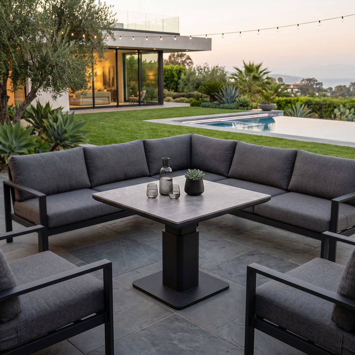 Outdoor seating area with modern grey cushioned chairs and the LUKA Adjustable Height Table featuring a sleek square tabletop in a serene backyard setting.