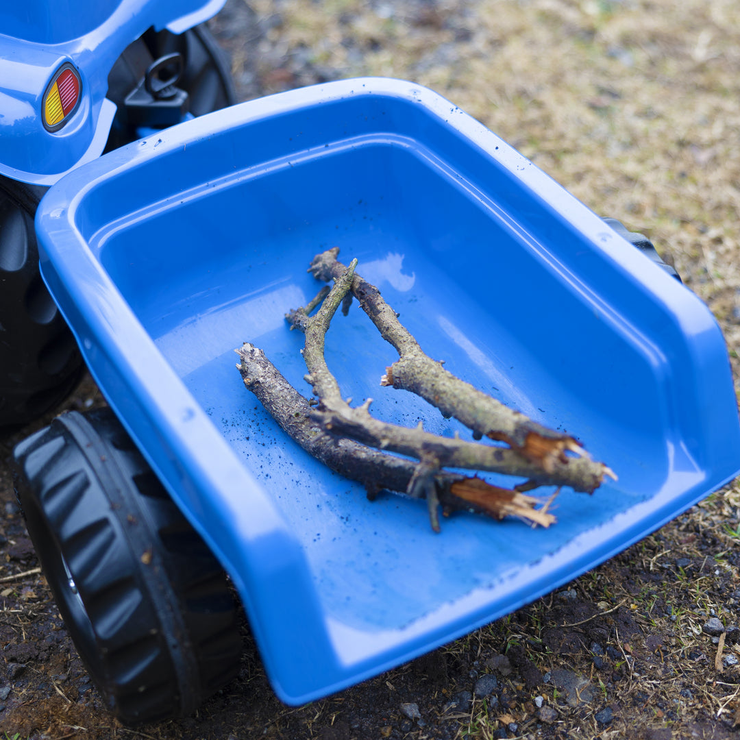 Blue New Holland Front Load Kid Tractor w/Trailer showing front loader with sticks inside on dirt ground.
