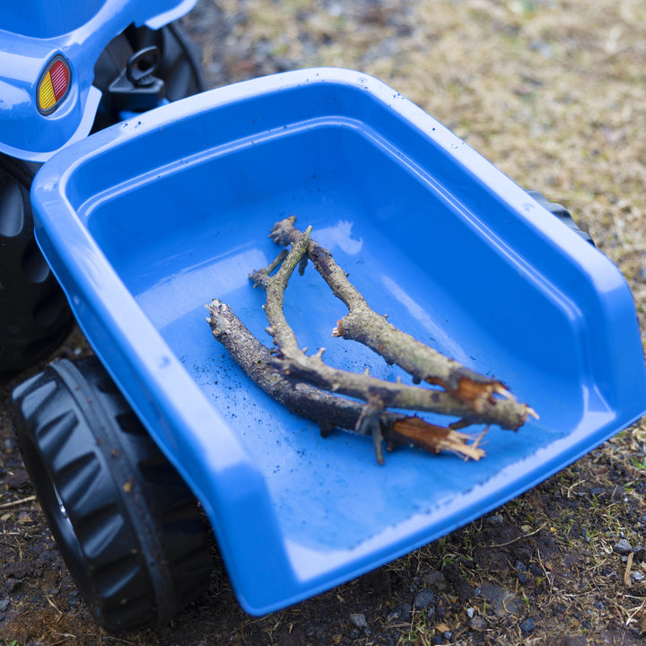 Blue New Holland Front Load Kid Tractor w/Trailer showing front loader with sticks inside on dirt ground.