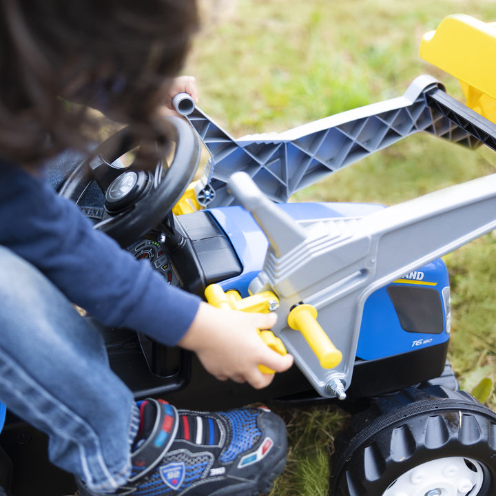 Child playing with New Holland Front Load Kid Tractor w/Trailer pedal tractor in a grassy outdoor setting.