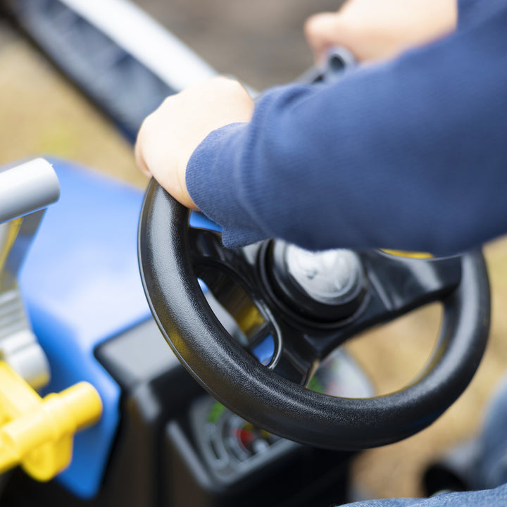 Close-up of child’s hands on steering wheel of New Holland Front Load Kid Tractor w/Trailer pedal toy vehicle.