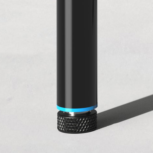 Close-up of a black cylindrical object standing on a textured black rubber base casting a shadow on a light gray surface