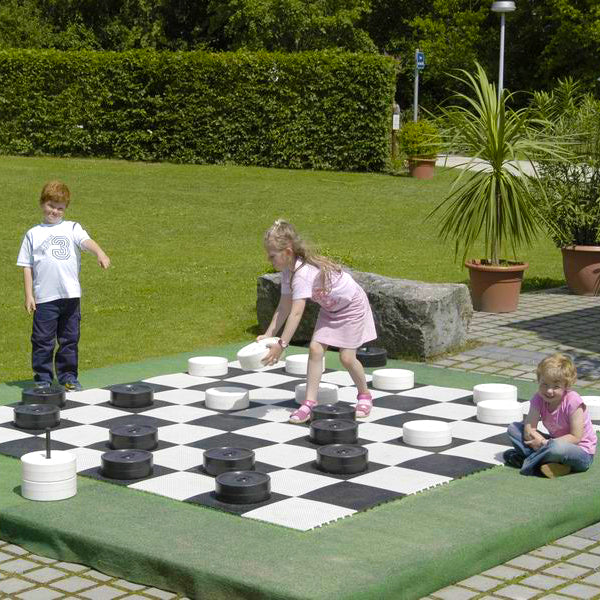 Children playing with Giant Checker Pieces on an oversized checkerboard outdoors in a garden setting.