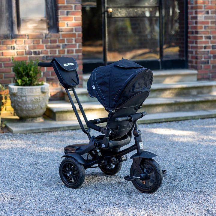 KETTLER Air Navigator 6-in-1 Tricycle in black with adjustable canopy, push handle, and sturdy wheels on gravel path.
