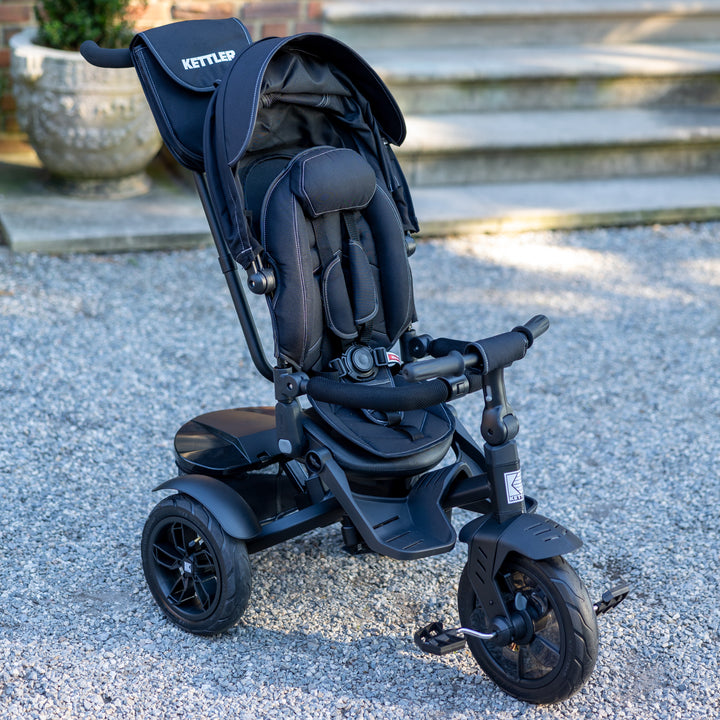 KETTLER Air Navigator 6-in-1 Tricycle in black with padded seat, safety harness, canopy, and parent handle outdoors.