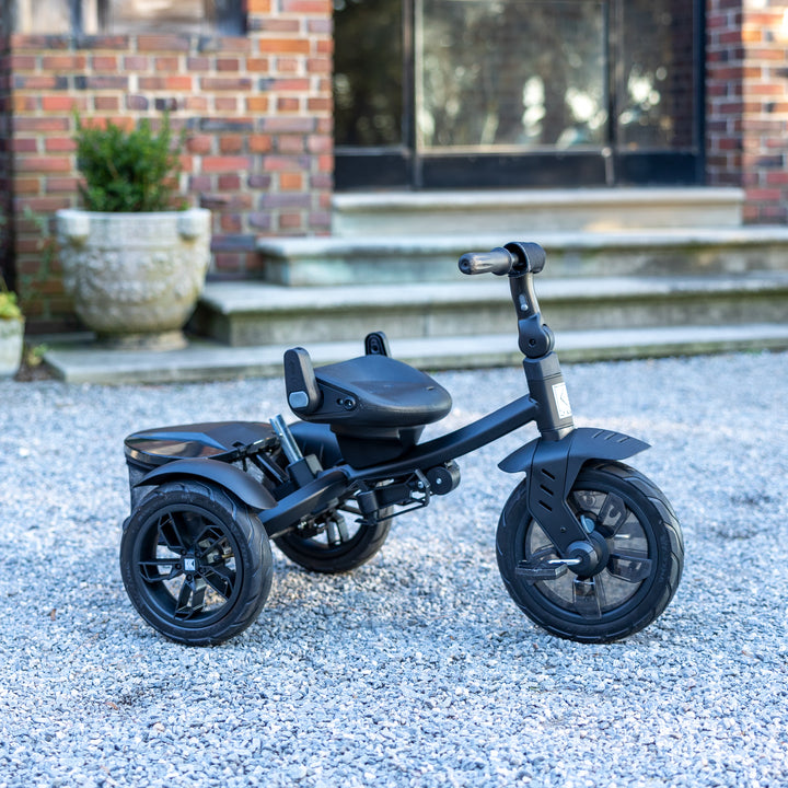 KETTLER Air Navigator 6-in-1 Tricycle in black with adjustable seat and pedals on gravel near brick steps.