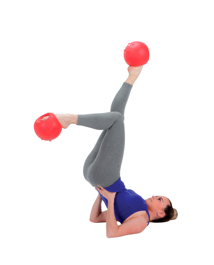 Woman exercising with red Gymnic Training Bowl Set held by feet in a leg raise workout pose on white background