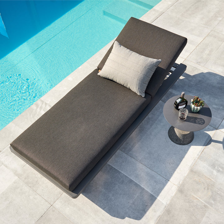 Fitz Roy Aluminum Lounger with lava aluminum frame and charcoal cushions by a poolside on stone tiles.