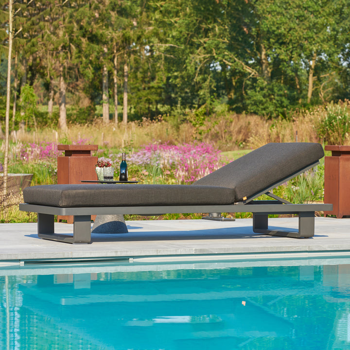Fitz Roy Aluminum Lounger with lava aluminum frame and charcoal cushions beside a pool in a garden setting.