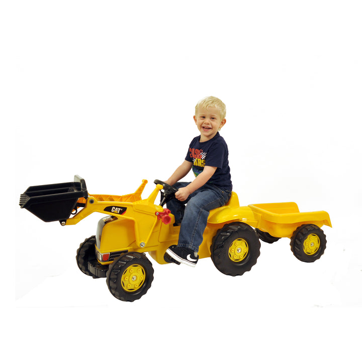 Young child riding the yellow CAT Kid Tractor With Trailer featuring a front loader and detachable trailer.