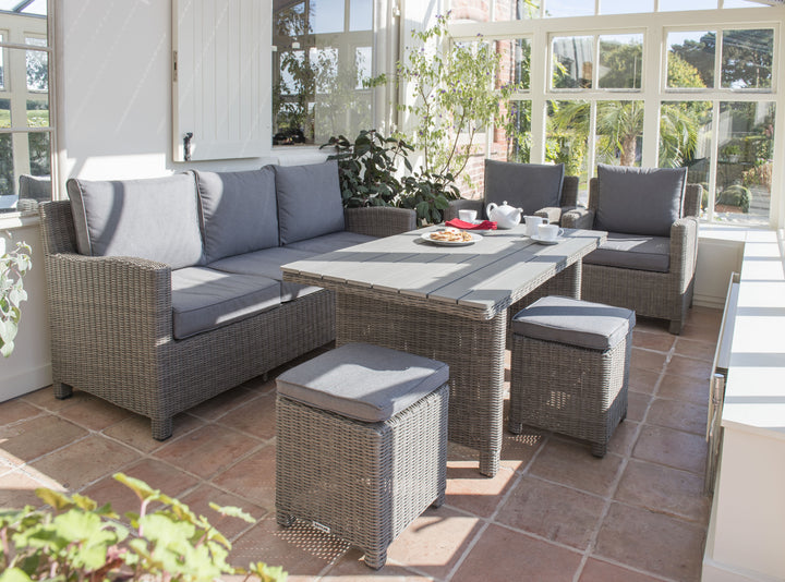 Palma Wicker Rattan Sofa set with gray cushions in sunlit indoor patio, featuring wicker dining table and foot stools.