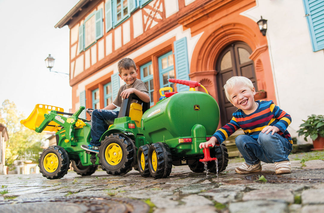 John Deere Water Tanker With Pump & Spray Gun attached to pedal tractor with kids playing outdoors by house.