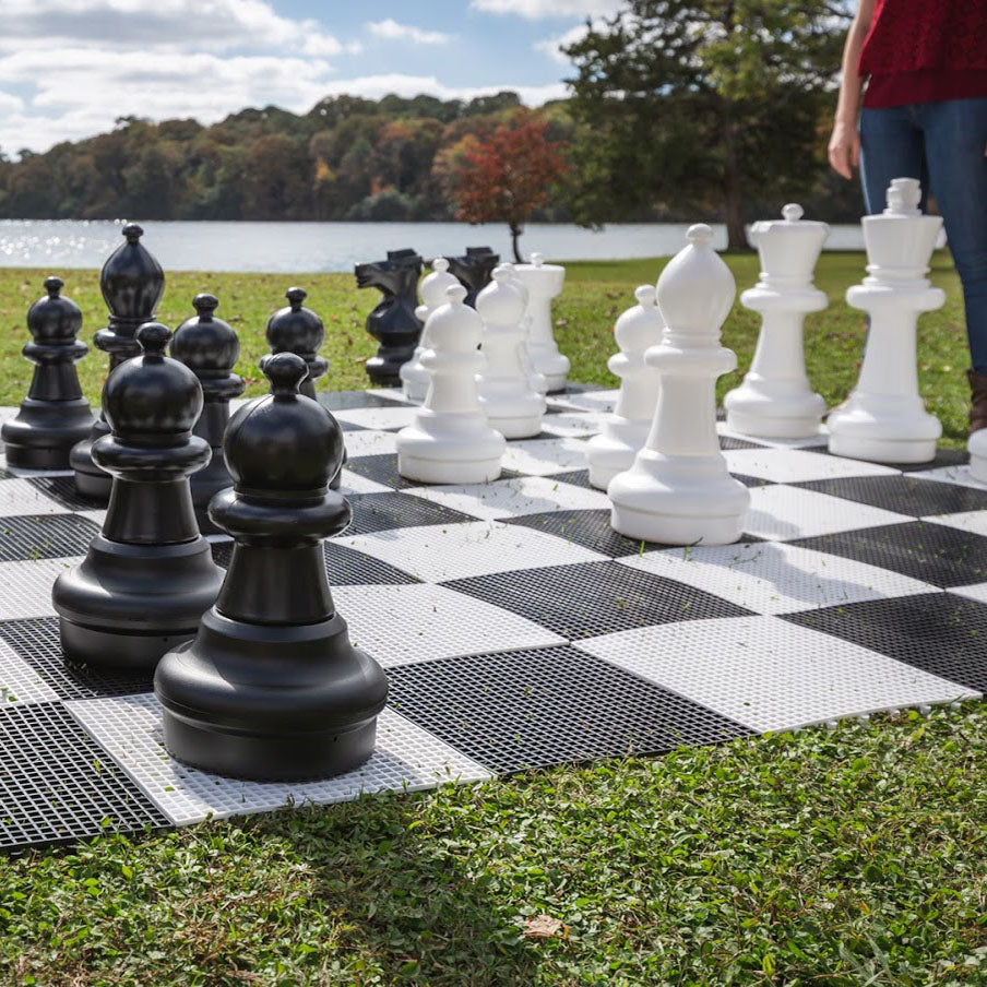 Giant Chess Set with oversized black and white resin chess pieces on large outdoor 10x10 game board by the lake.