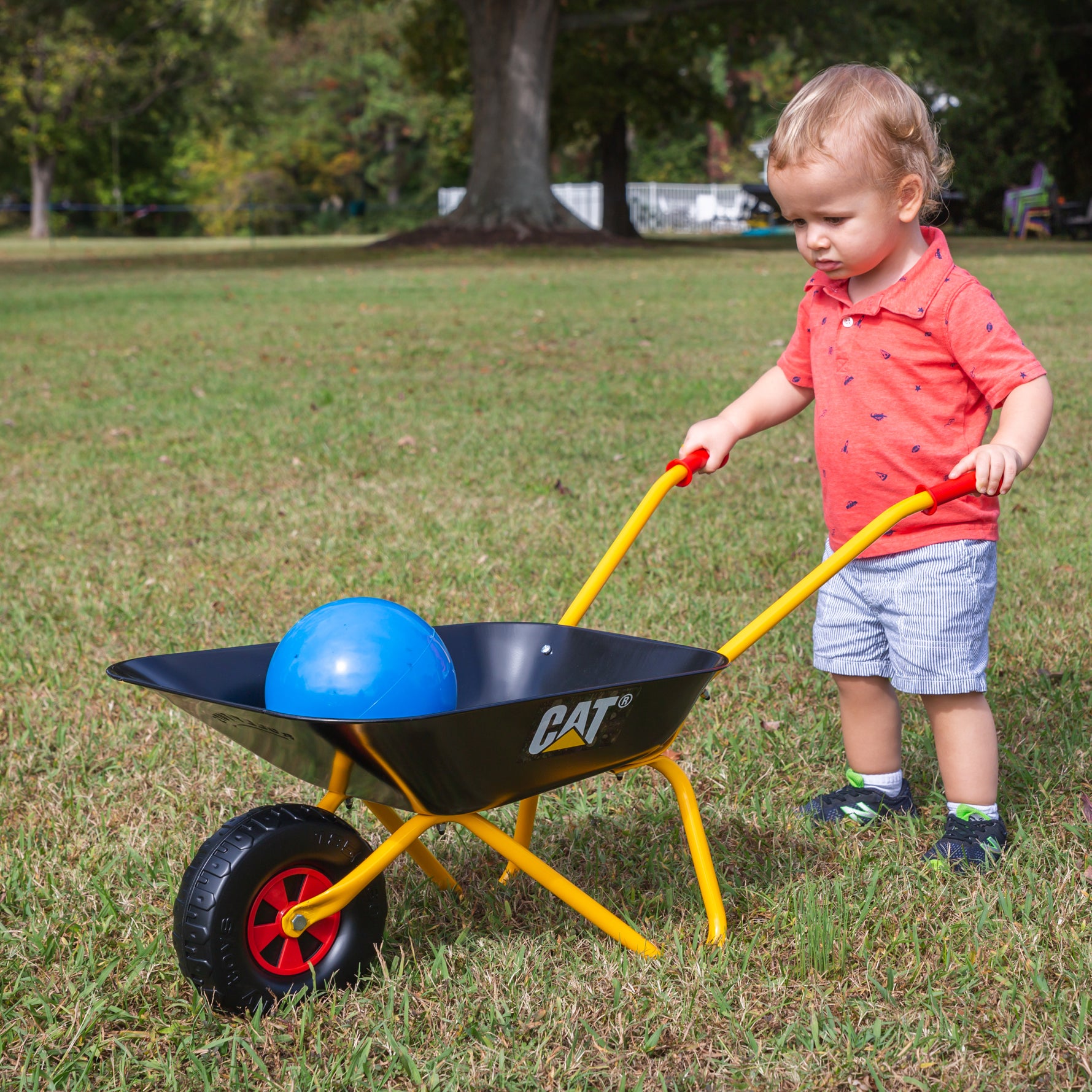 Lifestyle image of child using metal caterpillar wheelbarrow to haul load 