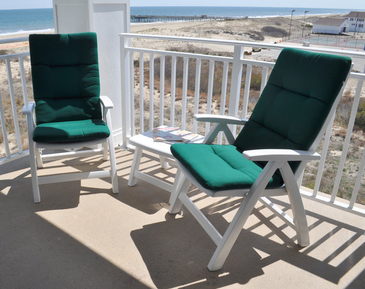Multi Position Hinged Chair Cushions in green on white outdoor chairs on a balcony overlooking a beach.