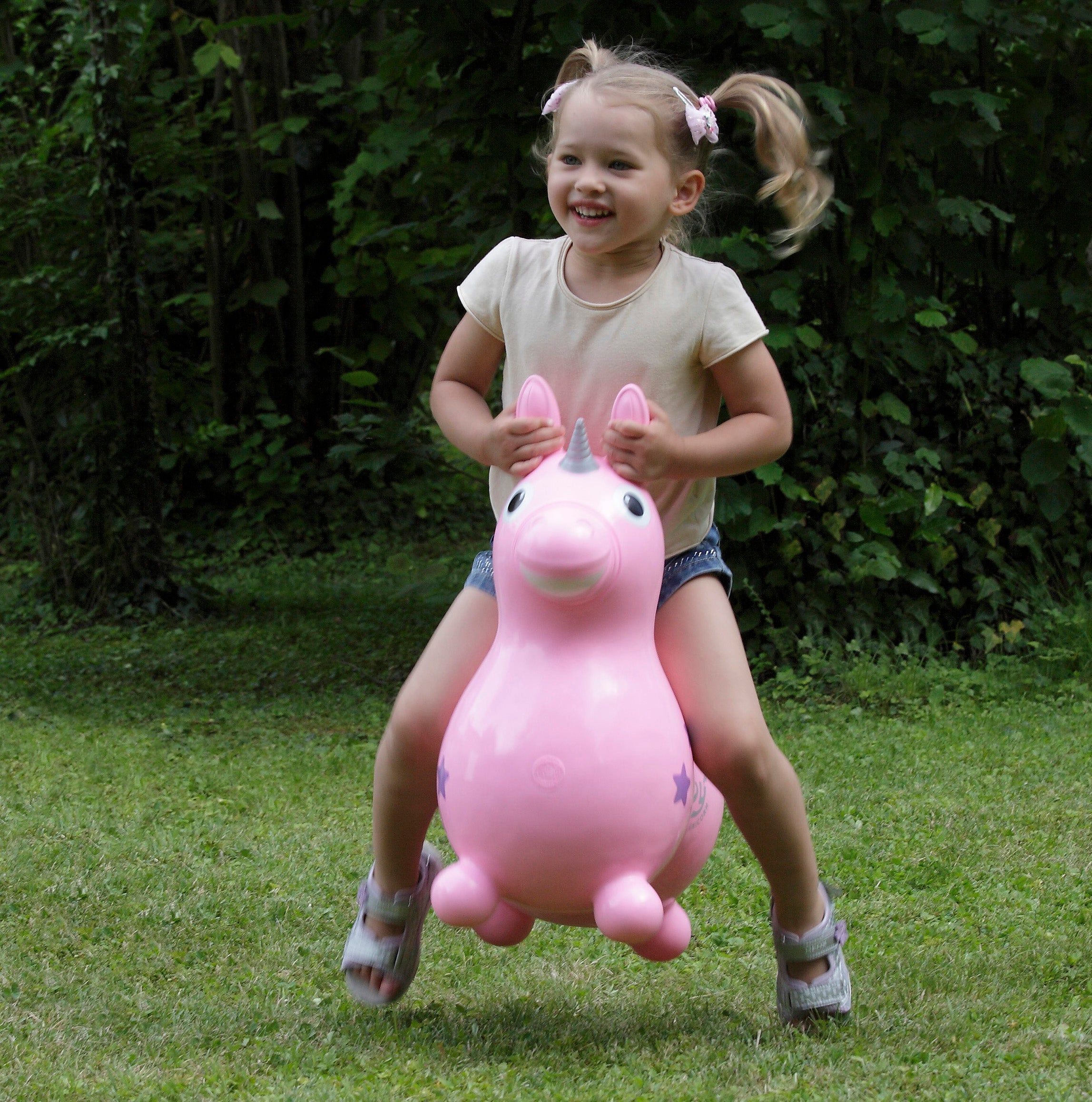 Lifestyle image of the pink Rody Magical Unicorn with little girl bouncing on it.