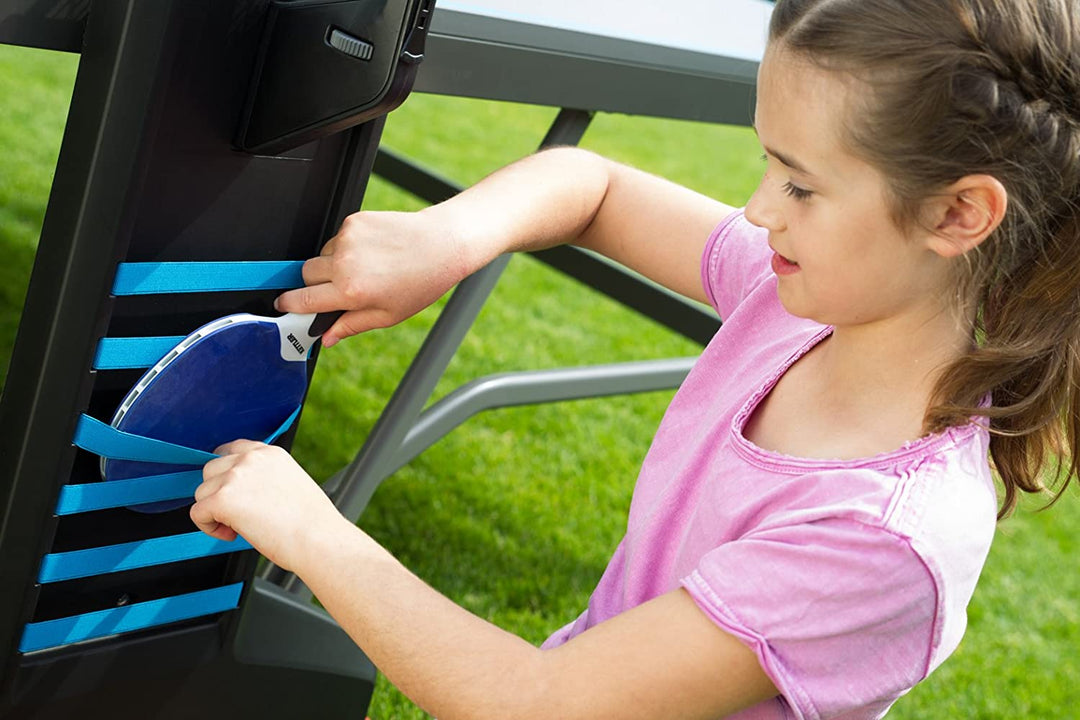 Outdoor 6 Table Tennis 4-Player Bundle showing a girl storing paddles in the table’s side slots outdoors.