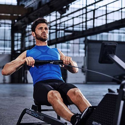 Man exercising on KETTLER Coach H2O Rower with water resistance in an indoor gym setting.