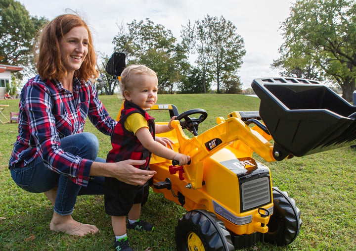 CAT Front Loader With Backhoe Pedal Tractor with child riding and adult supervising outdoors on grass lawn.