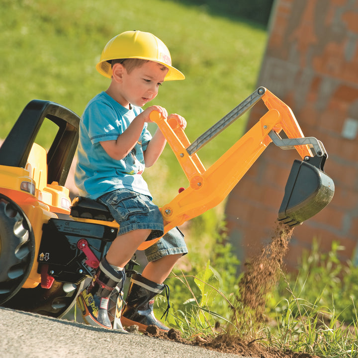 Child in yellow helmet playing with CAT Front Loader With Backhoe Pedal Tractor digging dirt outdoors on a sunny day