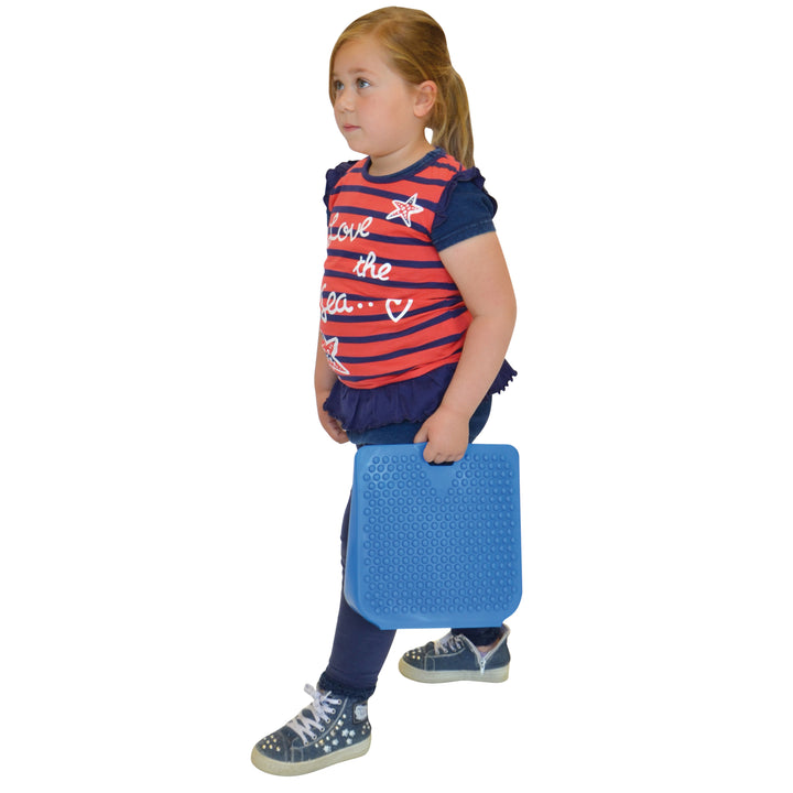 Child carrying a blue Gymnic Movin' Sit Jr. inflatable wedge for improved posture and focus in school chairs.