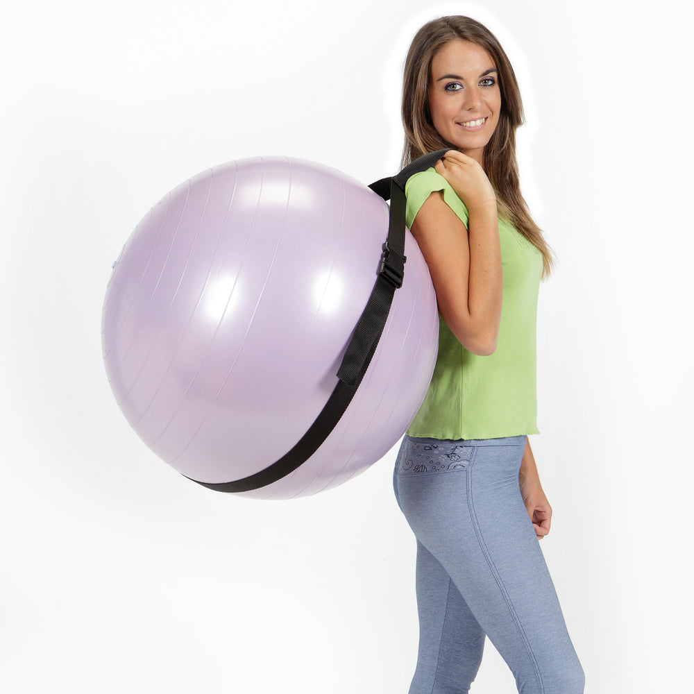 Woman carrying a purple fitness ball using the Gymnic Fitness Ball Carry Strap designed for 55 cm and 65 cm balls.
