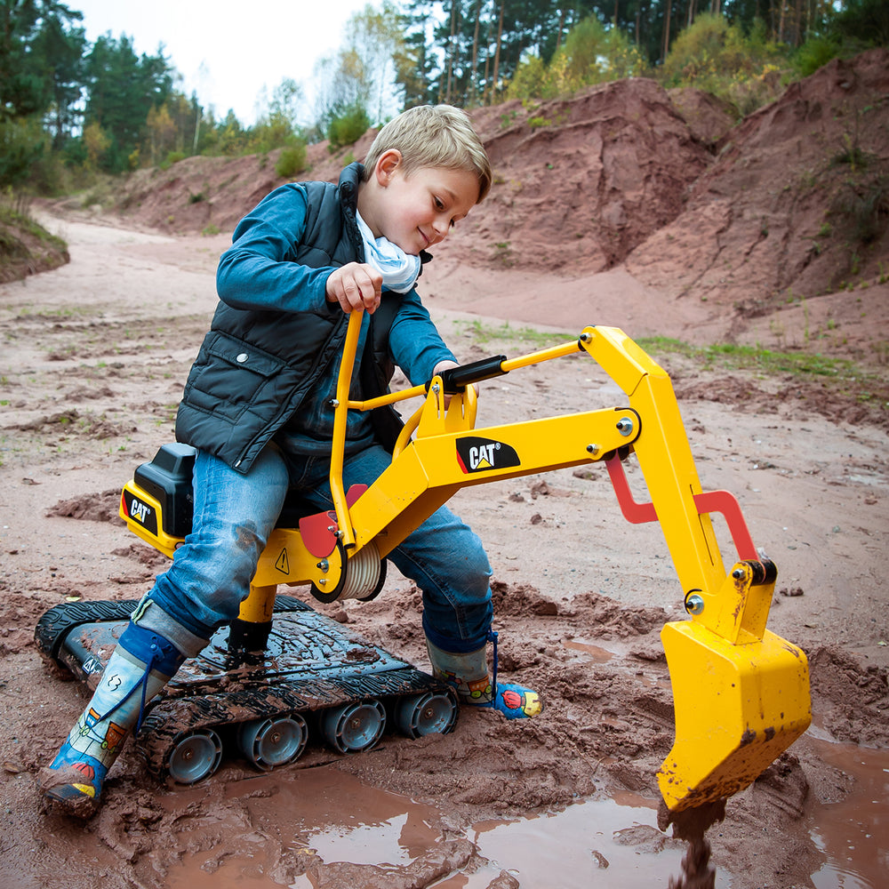 Child playing with yellow CAT Metal Digger toy with tracked wheels digging in muddy terrain outdoors