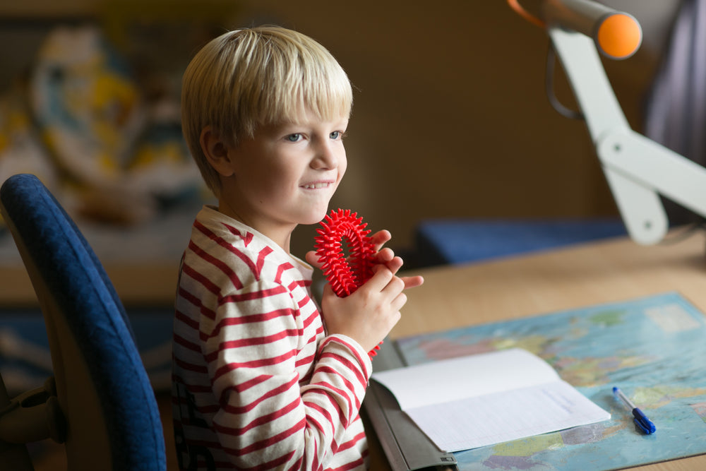 Child holding red Gymnic Aku Rings In Choice Of 4 Colors while seated at desk with notebook and map