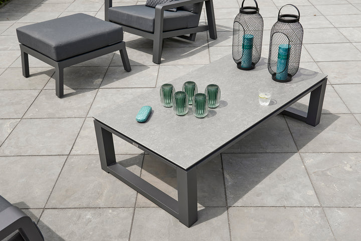 Primavera Coffee Table with aluminum frame and concrete look ceramic top on outdoor patio with decorative items.