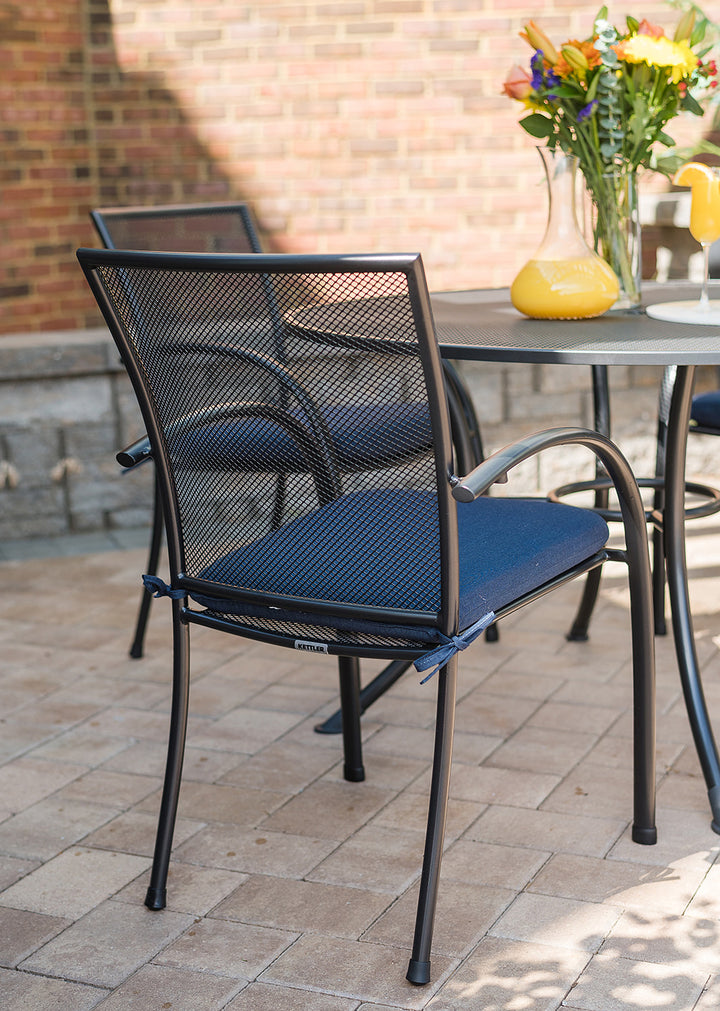 Pilano Wrought Iron Stackable Arm Chair set of 6 in iron grey with blue cushions on outdoor patio table.