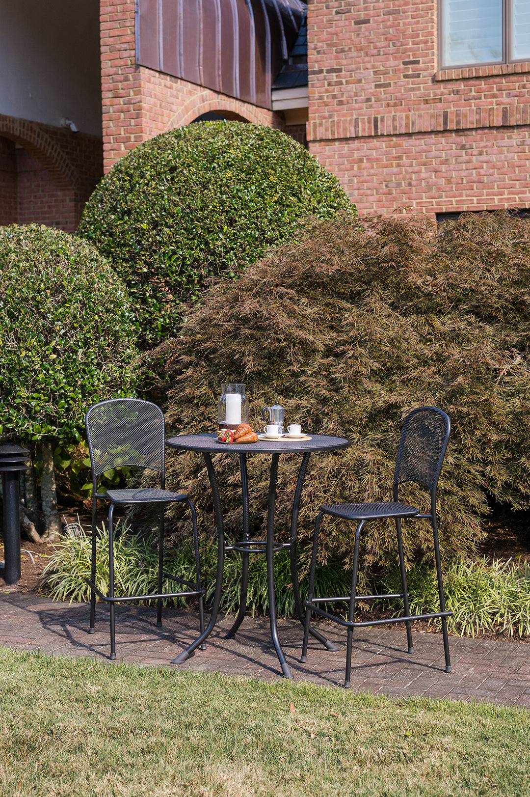 36-inch Round Mesh Bar Table with iron grey Electrotherm coated steel mesh top and two matching bar stools outdoors.