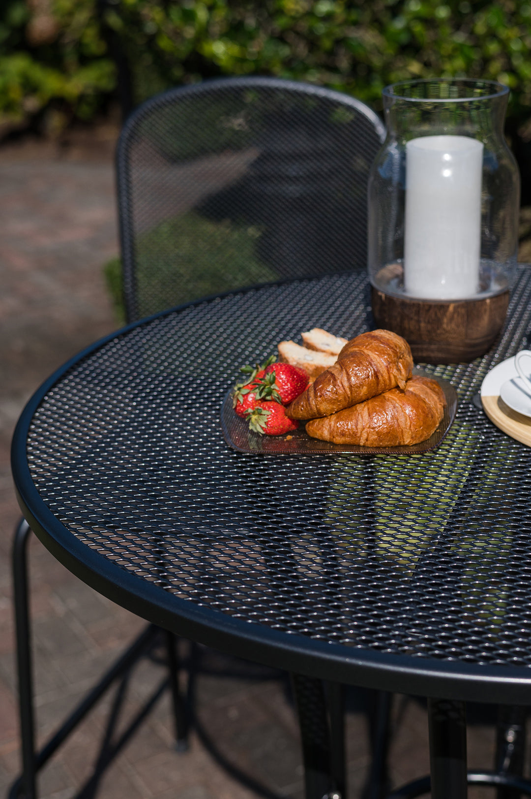 36-inch Round Mesh Bar Table in iron grey with wrought iron mesh top and croissants on plate outdoors