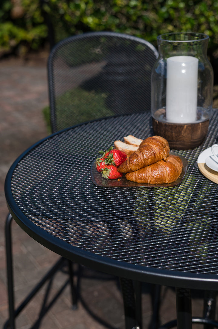 36-inch Round Mesh Bar Table in iron grey with wrought iron mesh top and croissants on plate outdoors