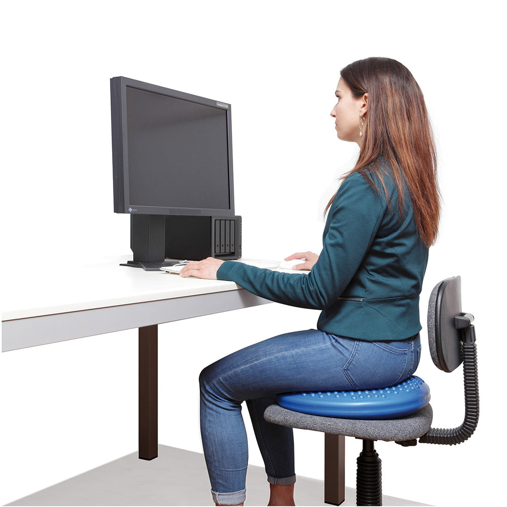 Woman sitting on a blue Gymnic Disc 'O' Sit cushion at a desk, promoting active seating and posture support.