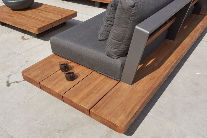 Fitz Roy Teak Corner Set showing teak side table, gray cushions, and aluminum frame on outdoor patio.