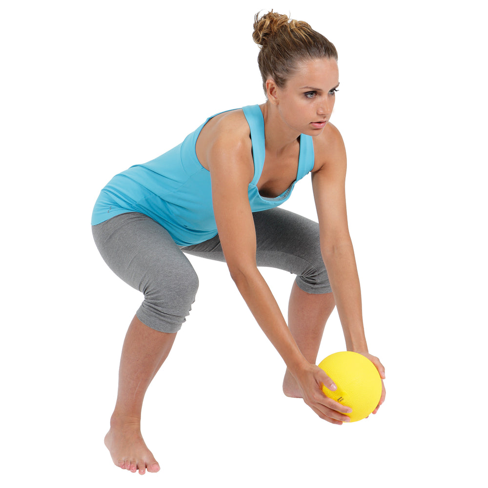 Woman in activewear holding a yellow Gymnic Heavymed Ball performing a squat exercise on a white background