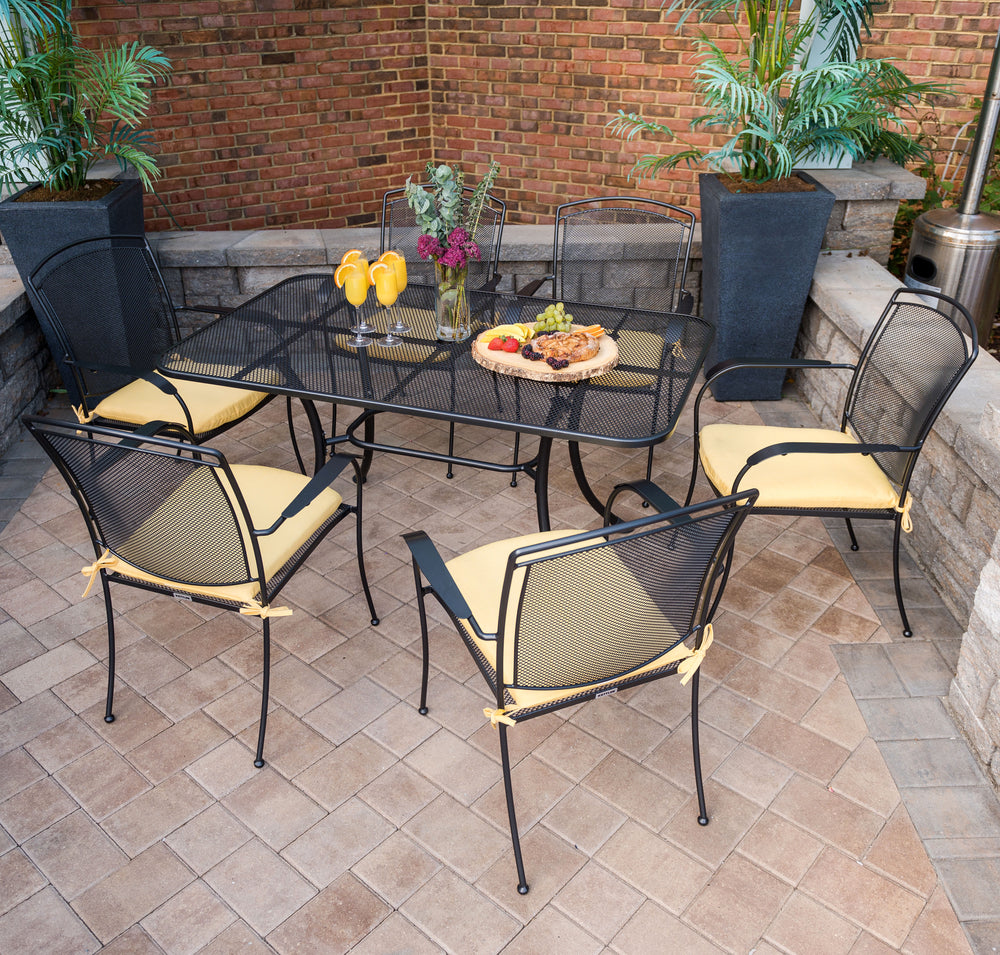 Henley 7-Piece Wrought Iron Mesh Dining Set with six stackable chairs and iron grey table with yellow cushions outdoors.