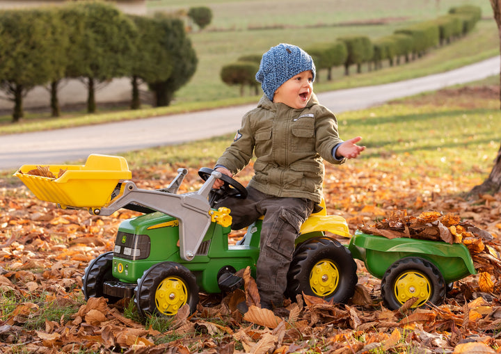 Child riding John Deere Pedal Tractor With Loader with detachable trailer on autumn leaves outdoors.