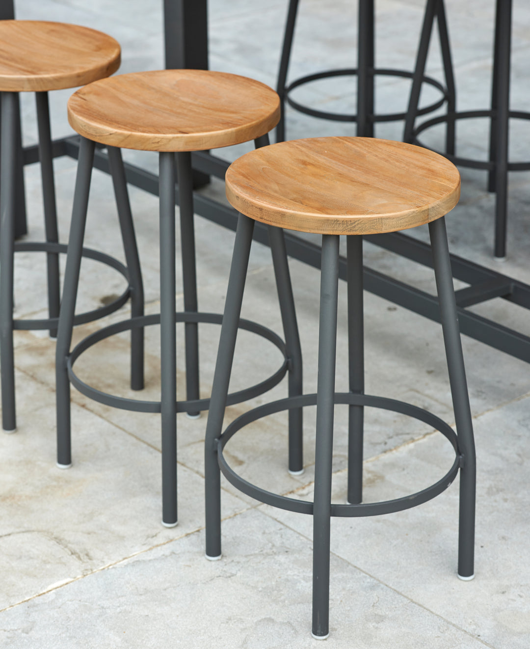 Canada Bar Height Dining Set with teak wood round seats and sturdy black metal frames on a tiled floor.