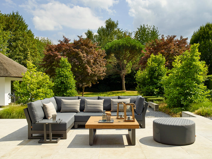 Nevada Right Sofa with charcoal cushions and powder-coated aluminum frame on a patio surrounded by trees and greenery.