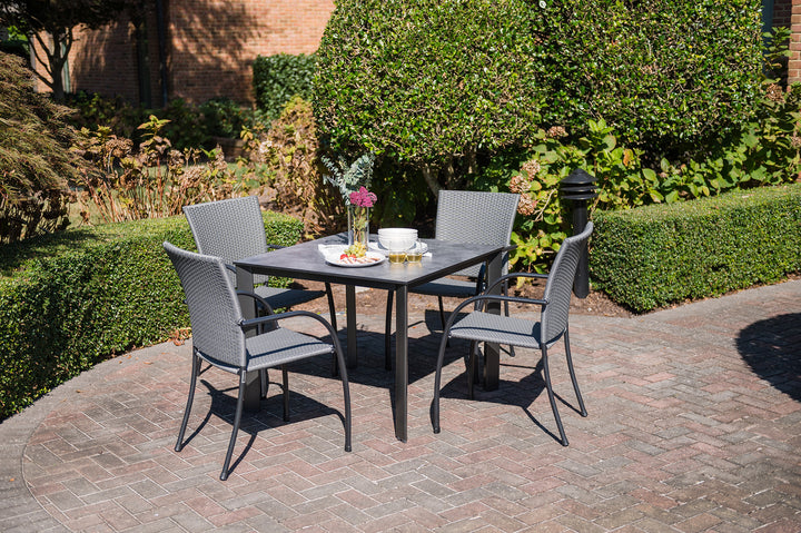 Pilano Woven Stackable Arm Chair set around a black dining table in a sunny outdoor patio garden setting.