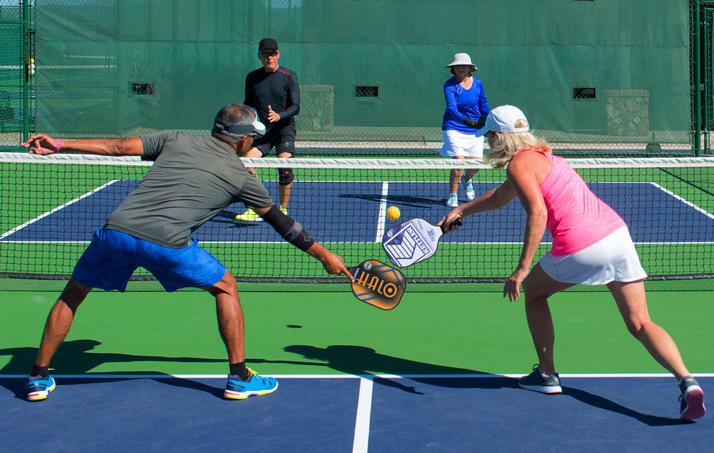 Two players hitting the ball with HALO® Pickleball Set paddles on a green and blue pickleball court.