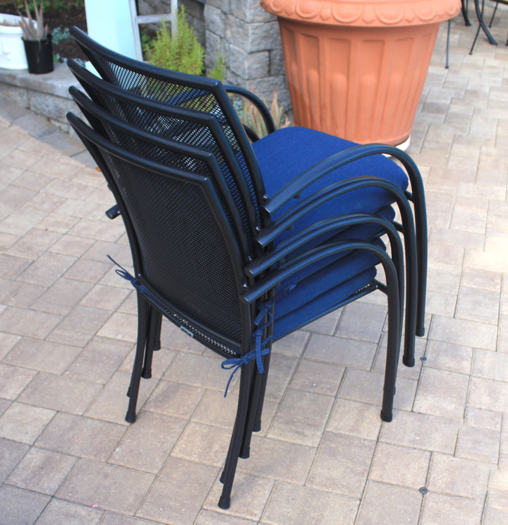 Pilano Wrought Iron Stackable Arm Chair - Set Of 6 stacked neatly outdoors with blue cushions on pavers.