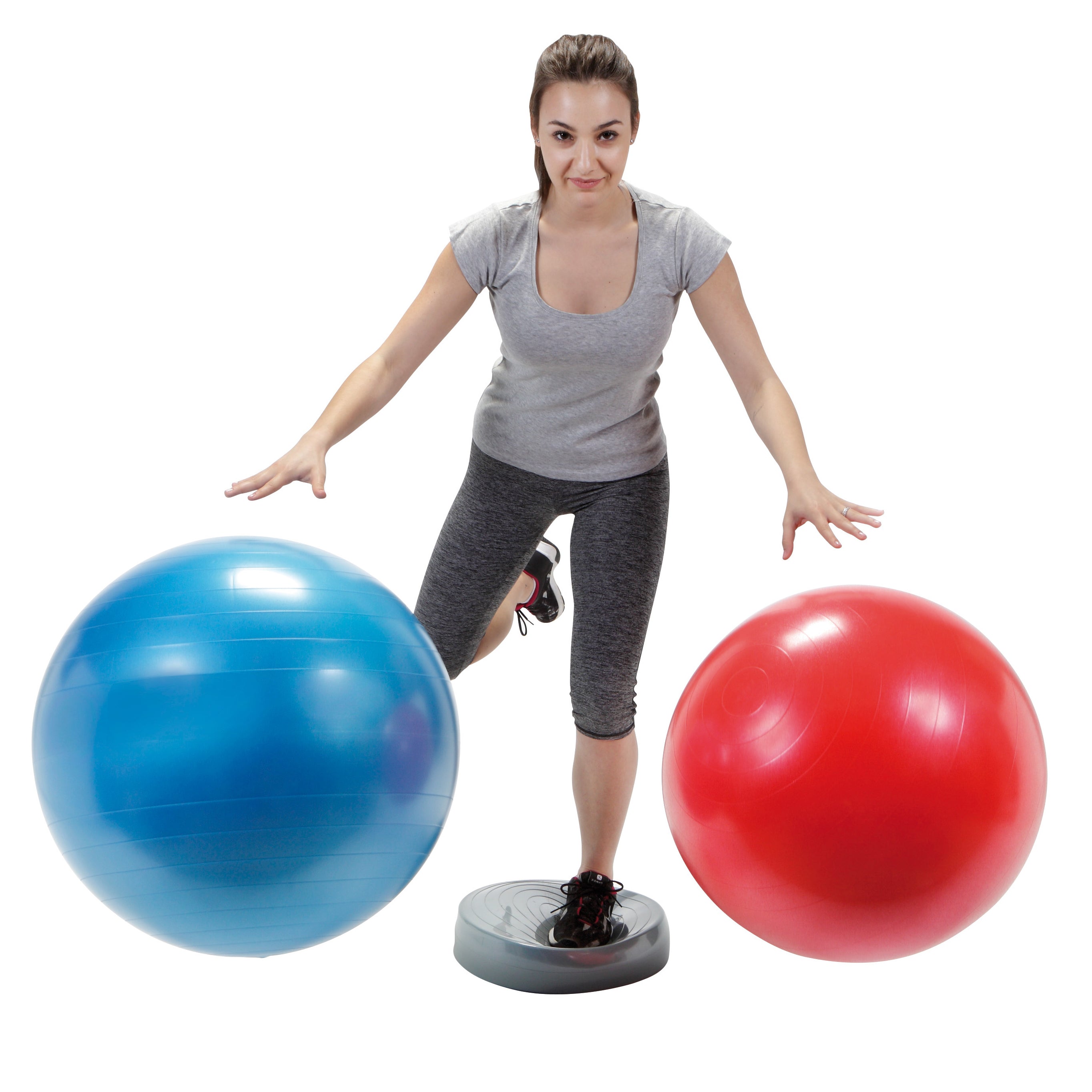 A woman balancing on a balance wheel while bouncing red and blue plus balls.