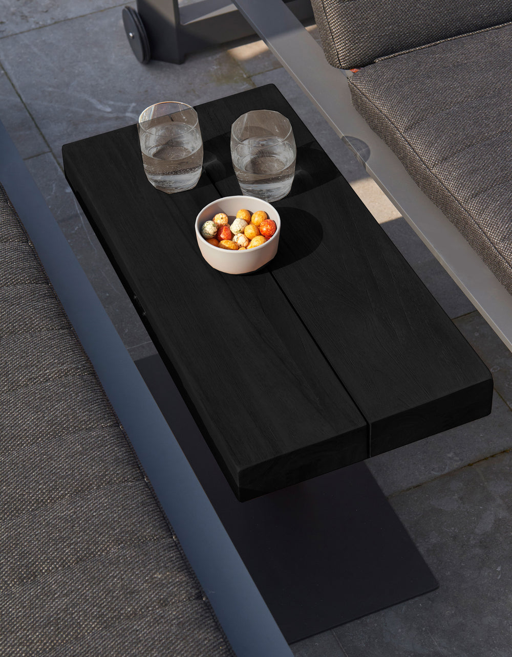 Fitz Roy Aluminum Side Table in Lava color with wide base holding glasses and a bowl between outdoor seating.