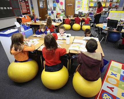 Gymnic Sit 'N' Gym Jr. Children's Sit-On Ball used by kids in classroom to improve posture and concentration with stability feet.