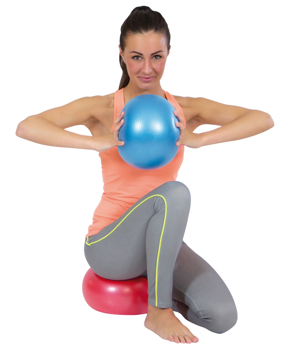 Woman exercising with a blue ball and sitting on a red ball using Gymnic Softgym Over Balls for Pilates and low-impact training.